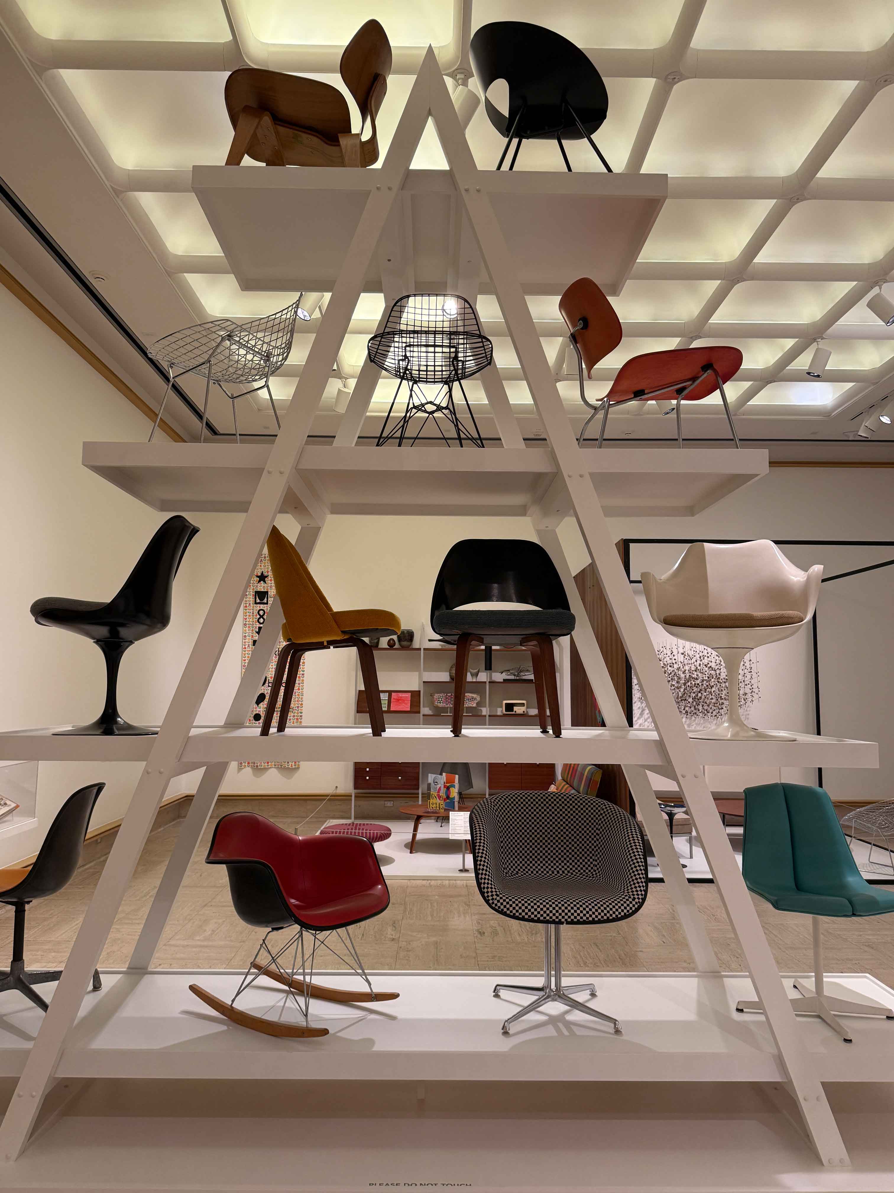 A museum-style shelving unit showcasing chairs of various styles, materials, and colors.