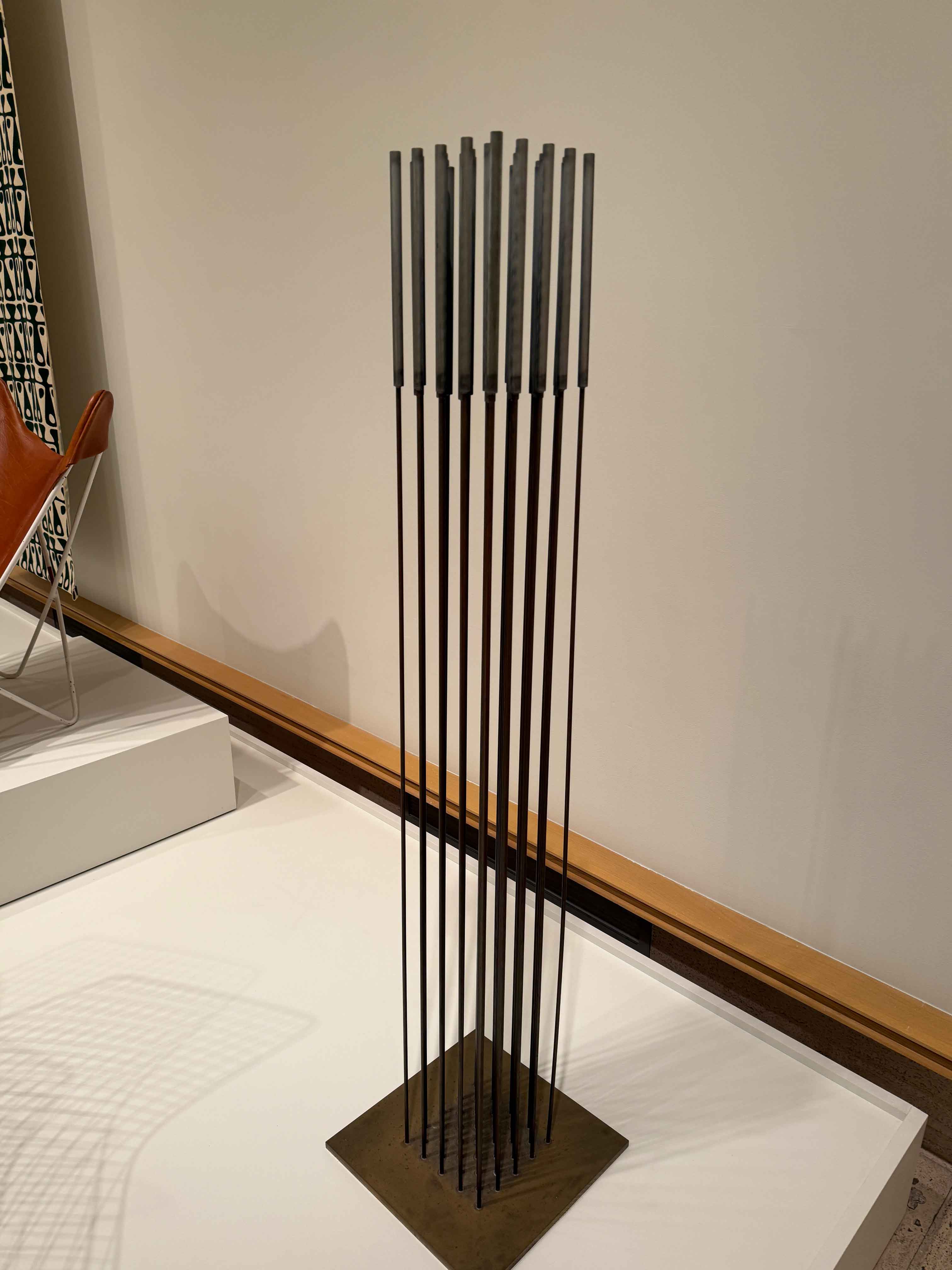 Vertical rods with rectangular metal tops, alongside a brown leather chair on a white platform